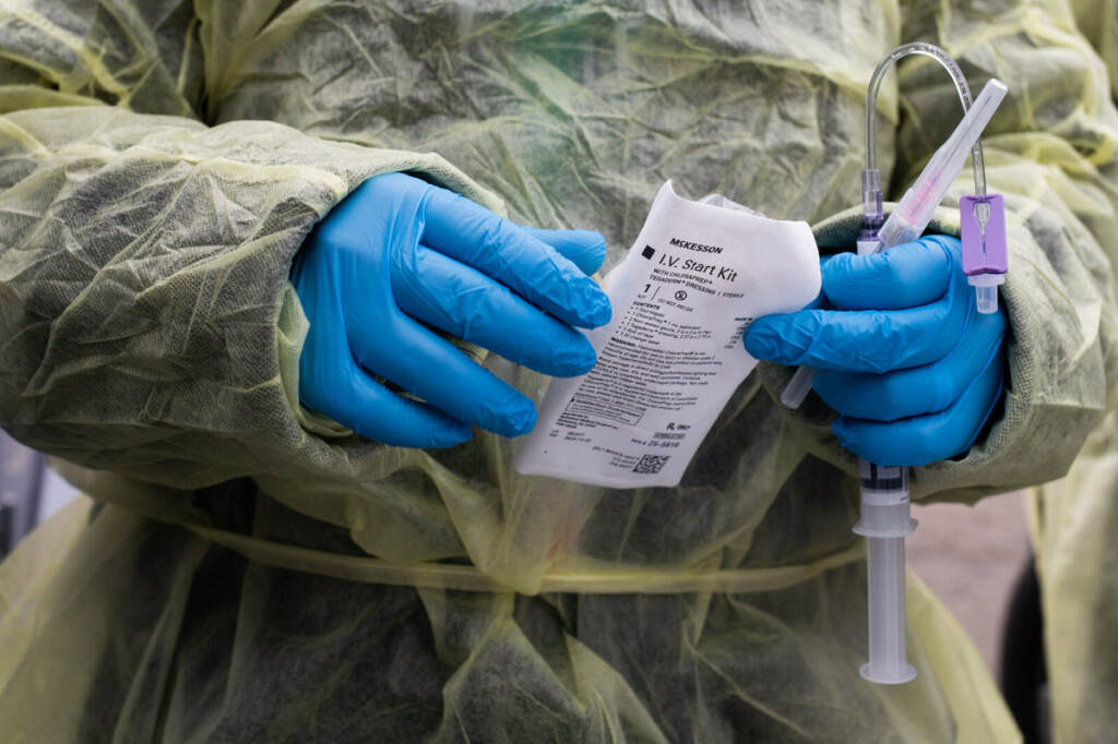 Monoclonal Antibody Treatment In Demand Amid Rise In Covid-19 Cases A close-up of a health care worker's hands, in blue gloves, handling an infusion for a patient at a drive-thru monoclonal antibody treatment.