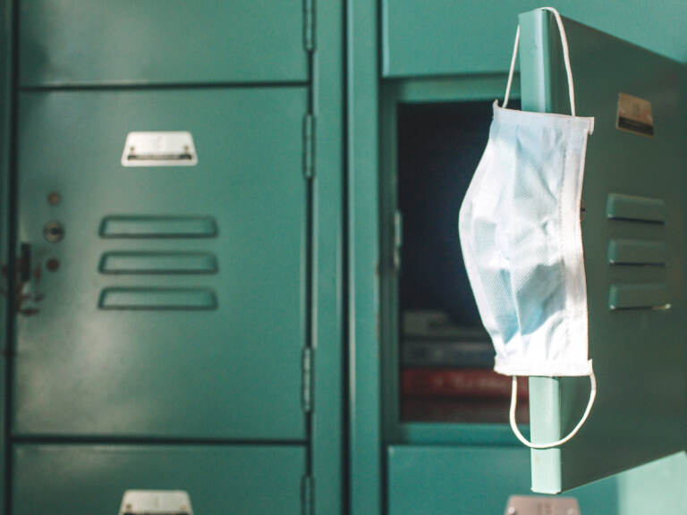 A surgical mask hangs from the open door of a green locker.