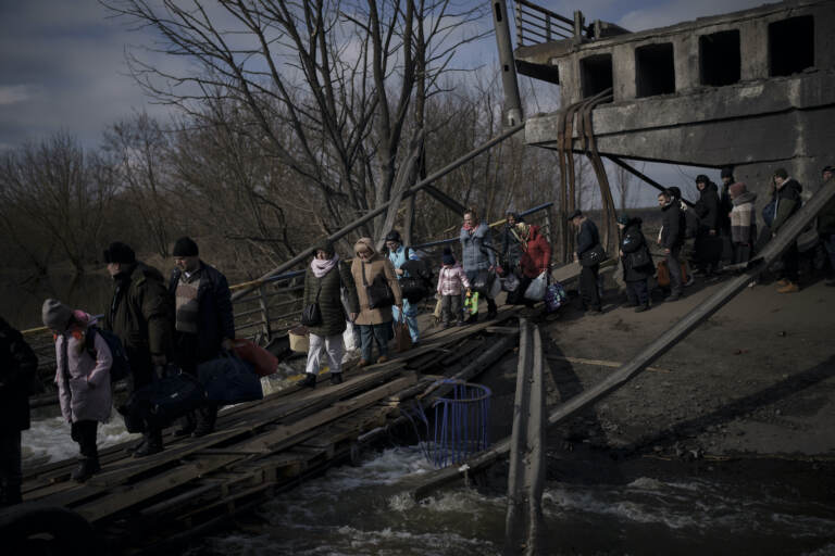 Ukrainians cross an improvised path under a destroyed bridge while fleeing Irpin