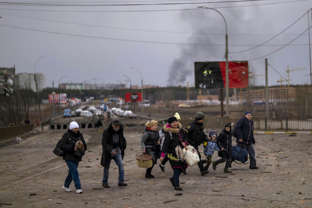 A Ukrainian police officer helps people as artillery echoes nearby while fleeing Irpin in the outskirts of Kyiv