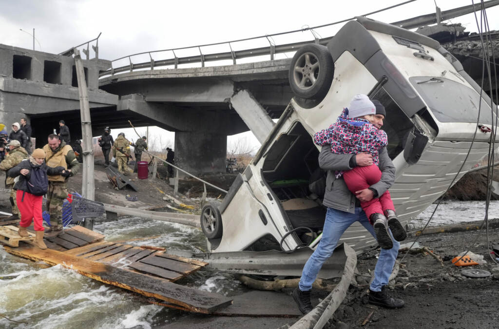 People cross an improvised path under a destroyed bridge while fleeing the town of Irpin