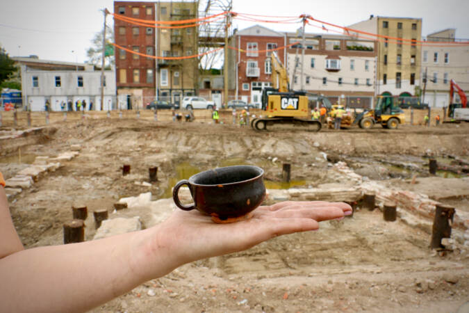 Archaeologist Caitlyn-Jean Ward holds a small porringer, a handled bowl, unearthed at the Columbus and Vine site. This one, made of locally produced redware, was likely a child's toy. (Emma Lee/WHYY)