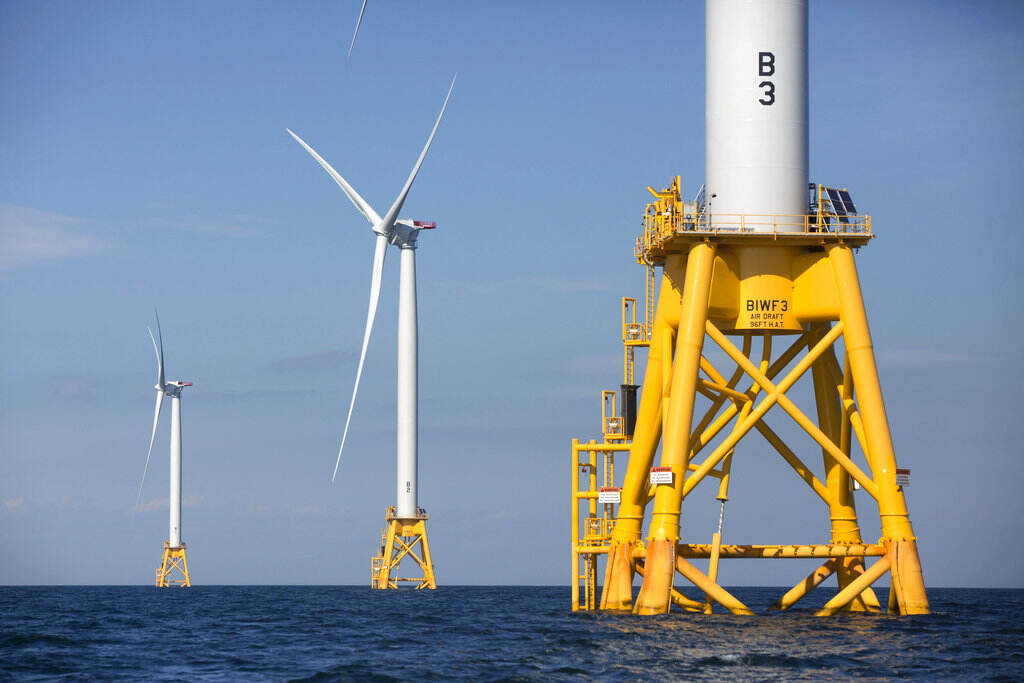 Offshore Wind Wind turbines are seen up close and in the distance in the ocean.
