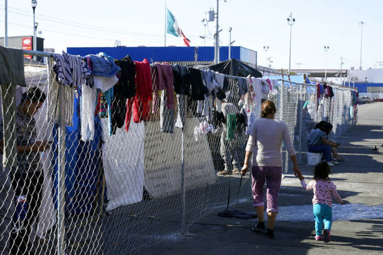 Migrants walk along a fence at a makeshift camp that is a temporary home for hundreds of migrants hoping to seek asylum in the United States at a pedestrian crossing on Nov. 8, 2021, in Tijuana, Mexico.