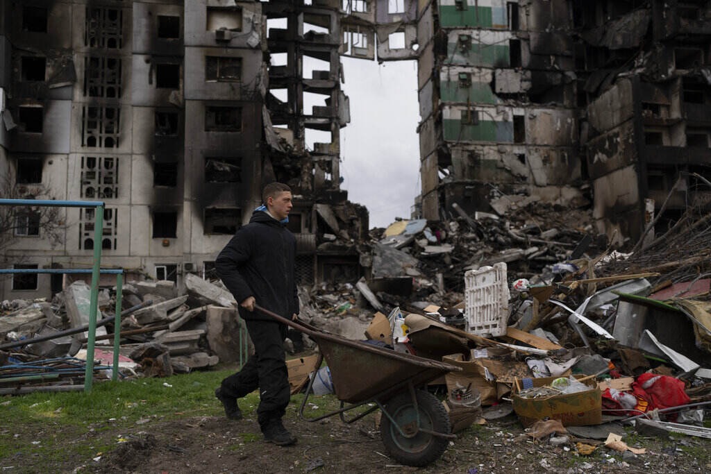 APTOPIX Russia Ukraine War A young man pushes a wheelbarrow in front of a destroyed apartment building in the town of Borodyanka, Ukraine, on Sunday, April 10, 2022. Several apartment buildings were destroyed during fighting between the Russian troops and the Ukrainian forces and the town is without electricity, water and heating.