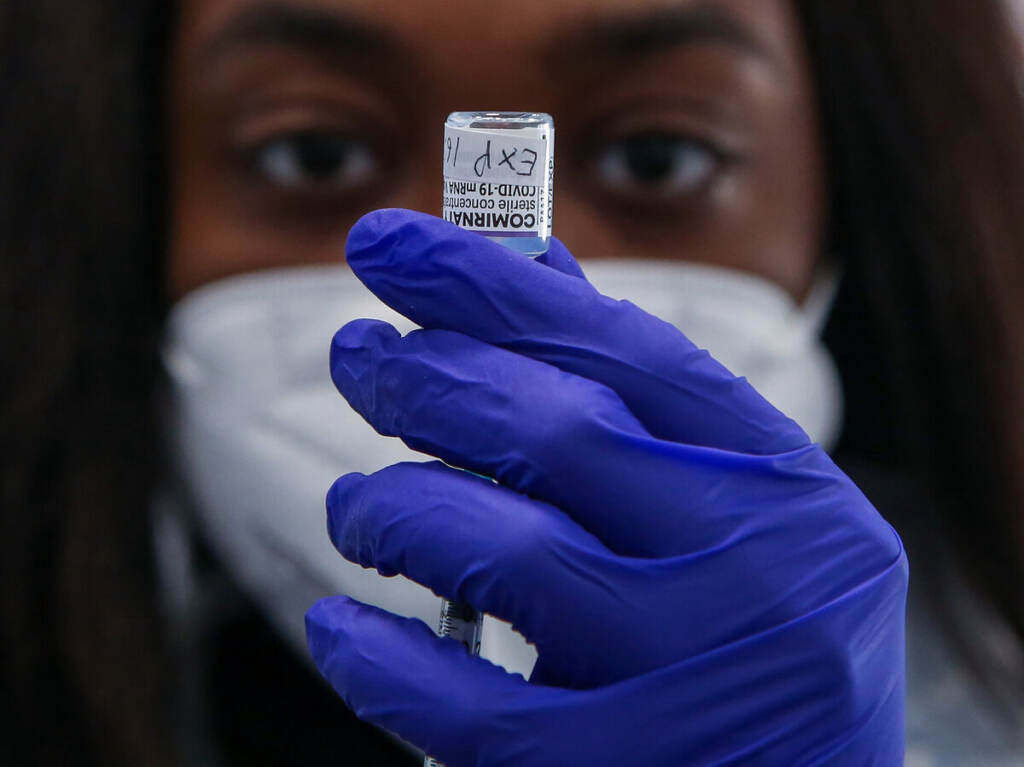 A NHS vaccinator draws the Pfizer COVID-19 second booster A medic wearing a facemask and dark blue gloves holds up a vaccine container.