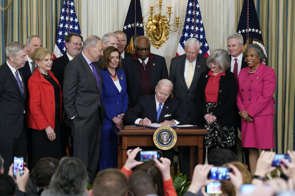 President Joe Biden signs the Postal Service Reform Act of 2022 in the State Dining Room, surrounded by elected officials