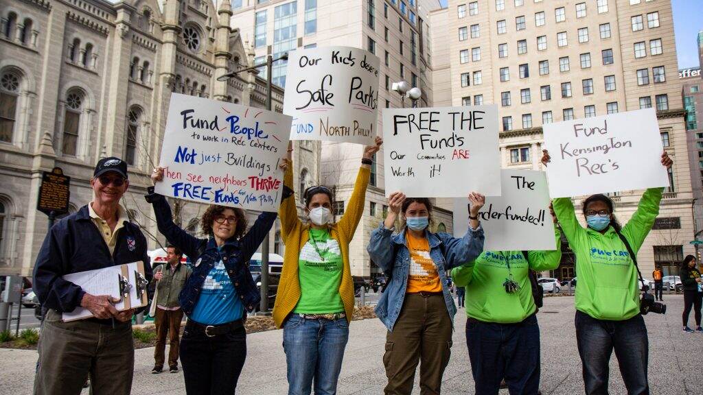 Protesters hold up signs in front of City Hall.
