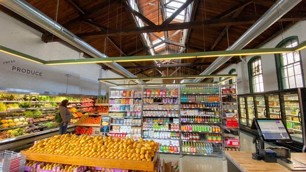 riverwardsproduce-oldcity18-1024×576 Fresh produce and stocked shelves of the grocery store, Riverwards Produce, are visible.