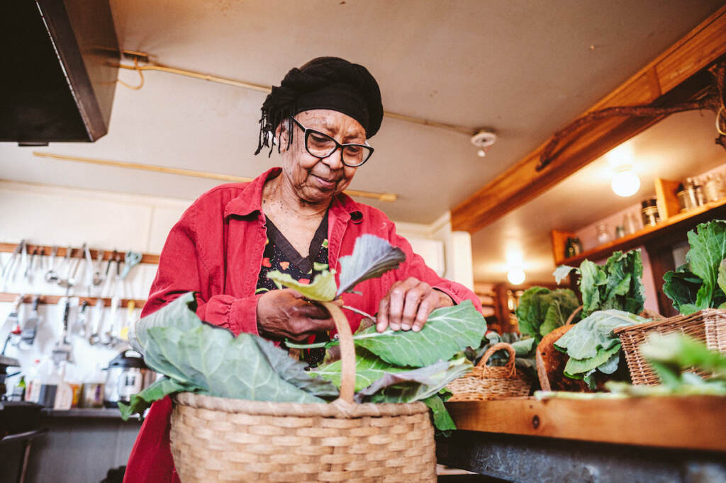 Ira Wallace Ira Wallace, wearing a red jacket, takes a piece of collard greens in the basket before her.