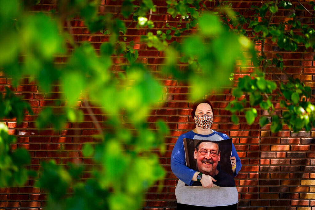 Sara Atkins poses for a photo, in Wynnewood, Pa., Tuesday, May 10, 2022, while holding a pillow with an image of her father Andy Rotman-Zaid, who died of COVID-19 in December 2020. She channels her grief into fighting for global vaccination and better access to health care to honor her father.