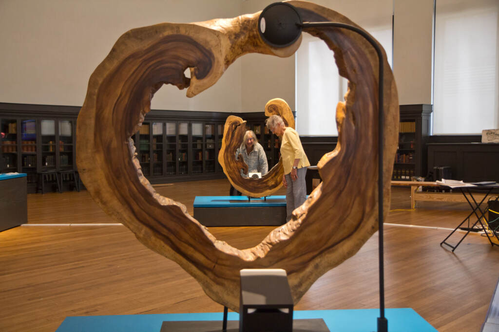 2022 05 26 k paynter the river feeds back (1 of 1) Two artists are visible in the background, with a wooden object from the exhibition in the foreground.