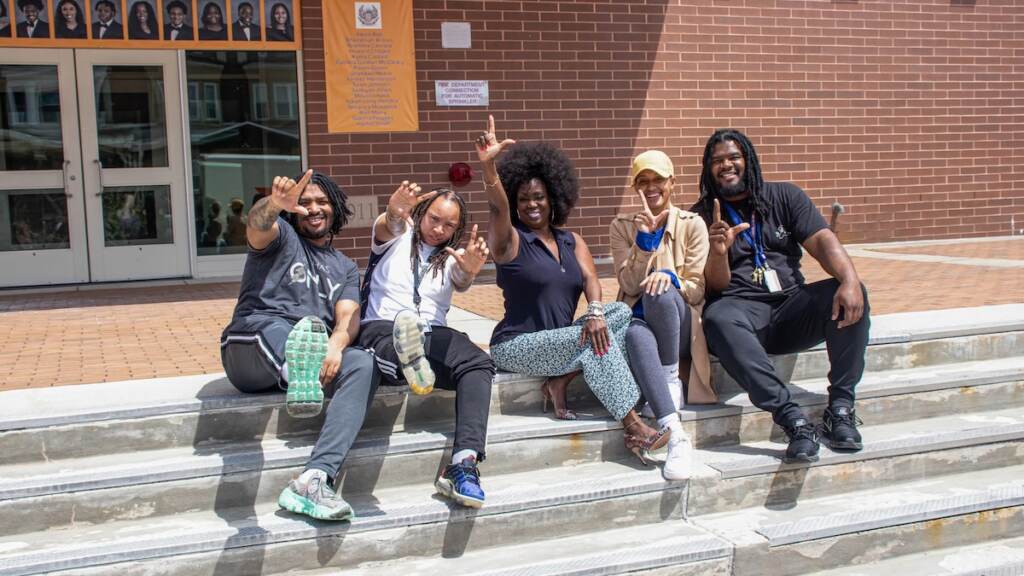From left- Jean-Claude Forte, Yaseemah Foster, Brittney Smith, and Robert Green. They are flashing the “L” Lamberton sign Marla Travis, center, on the steps of West Philadelphia High School, where she is the principal, with four of her former students at Lamberton High who are now teachers at West Philadelphia. From left: Jean-Claude Forte, Yaseemah Foster, Brittney Smith, and Robert Green. They are flashing the “L” Lamberton sign. (Tyriq Williams, student, West Philadelphia High School)