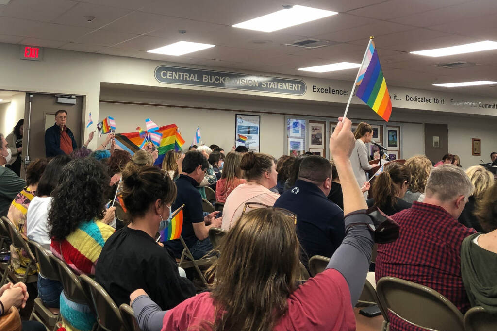Parents-and-students-waved-Pride-flags-in-the-air-as-Lena-Barnhat,-of-Doylestown,-said-_schools-should-not-be-a-place-for-promoting-sexuality._-Emily-Rizzo-_-WHYY-News School board meeting attendees wave LGBTQ pride flags