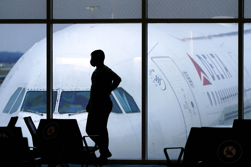 Flight Cancellations Memorial Day Weekend A silhouette of a person standing in an airport is visible, with a plane visible in the background, outside the window.