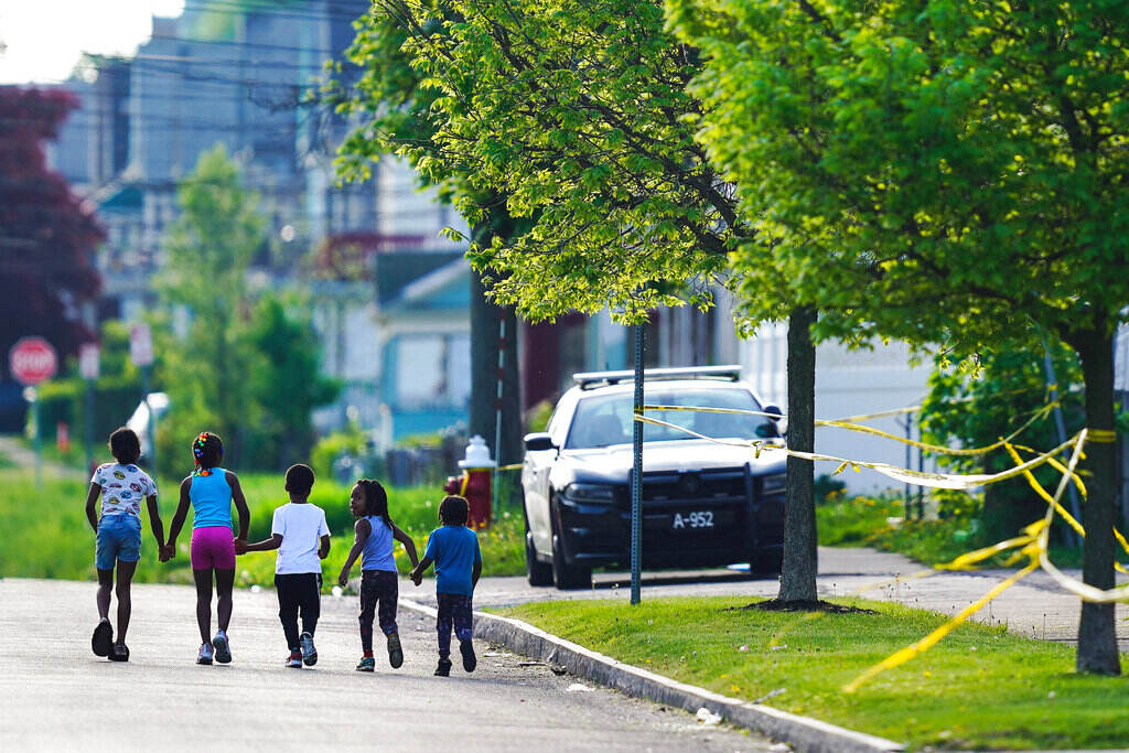 Buffalo Supermarket Shooting-School Counselors Children walk hand-in-hand down a tree-lined street, with yellow crime tape visible in the corner.