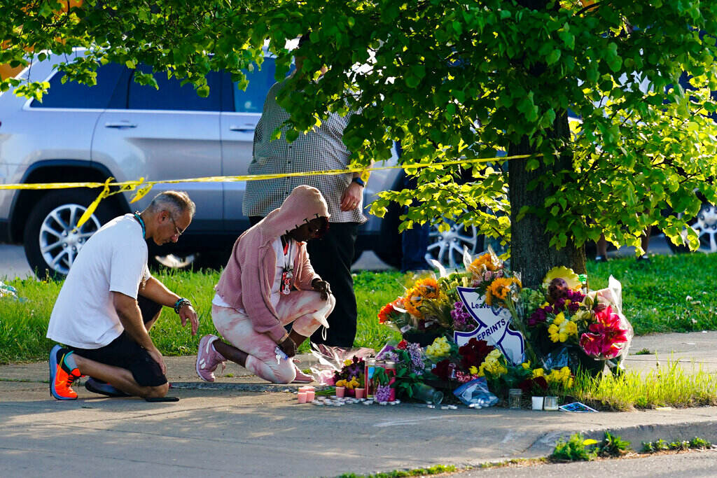 Two people kneel on the ground in front of a memorial made of flowers.