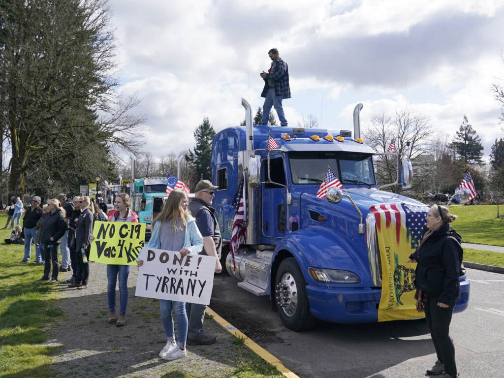 Virus Outbreak Washington Protest People hold signs as they stand near parked semi-trucks during a protest against COVID-19 vaccine mandates