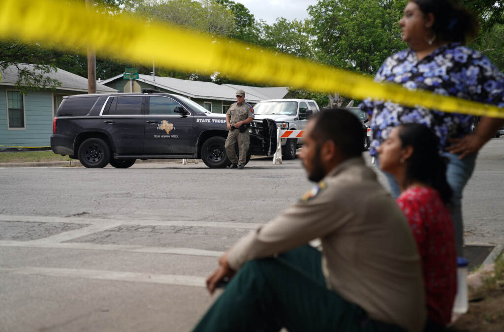 People sit on a sidewalk next to crime scene tape