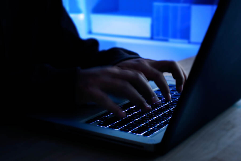 A computer programmer prints a code on a laptop keyboard. Close-up of someone's hands typing on a laptop in a dark room.