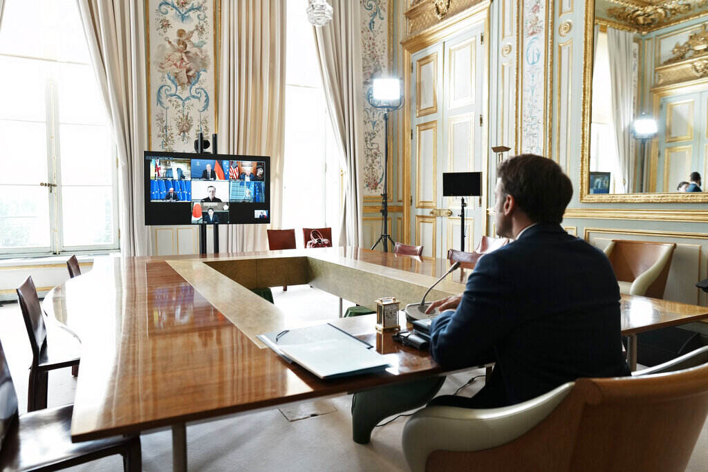 French President Emmanuel Macron is seen from behind, seated at a table, participating in a video conference with leaders of the other G7 countries.
