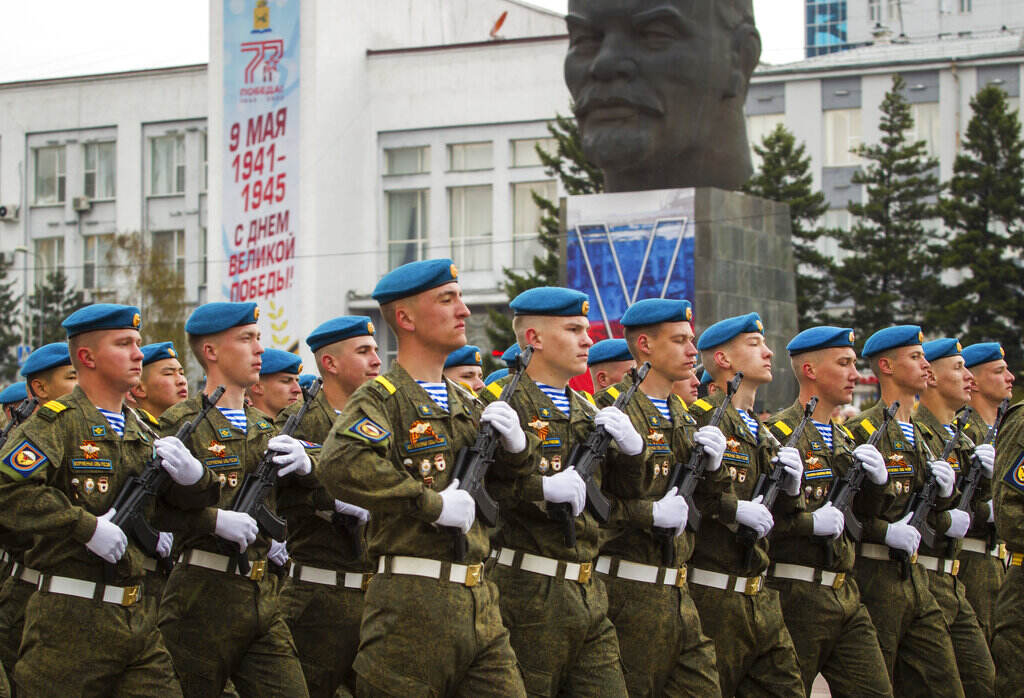 Russia Victory Day Parade Russian soldiers march in one line, with a statue in the background.