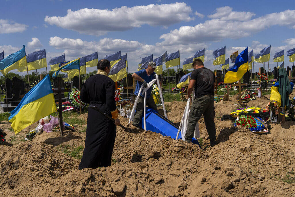 APTOPIX Russia Ukraine War People gather around a grave in a dirt field with numerous Ukrainian flags flying.
