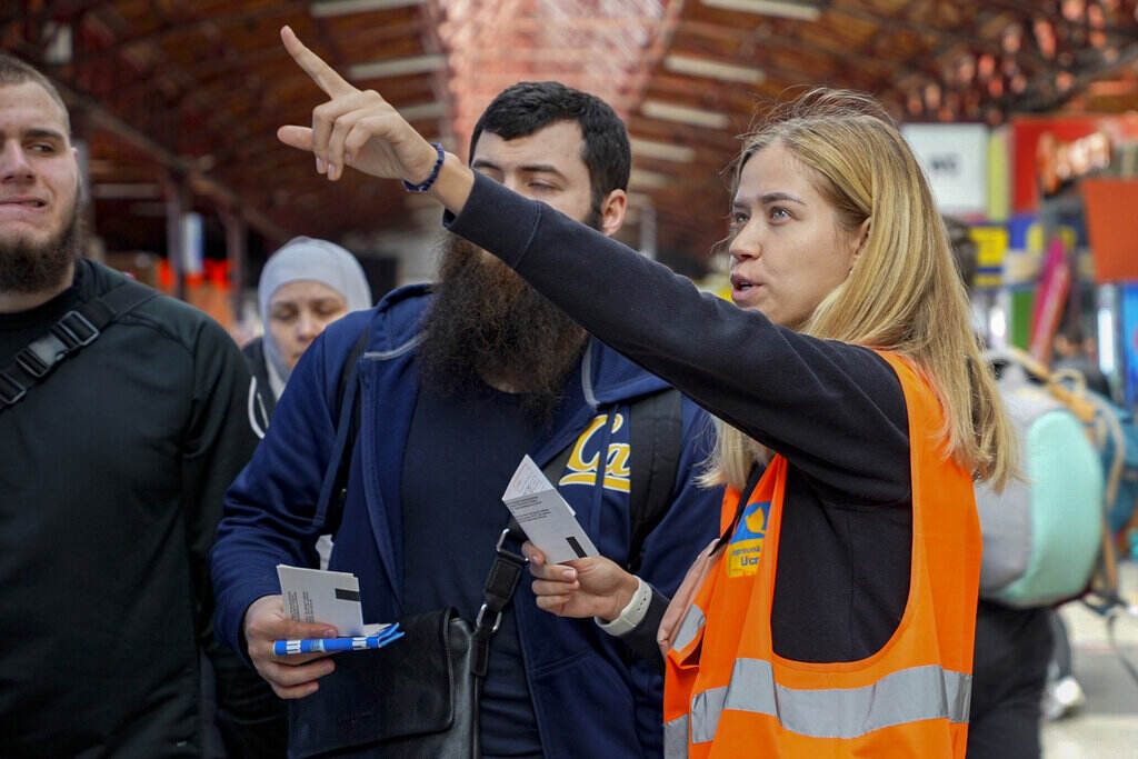 Romania Ukraine Russia War Refugees A Urkrainian volunteer wearing an orange vest gestures in the distance as she stands next to a group of people.