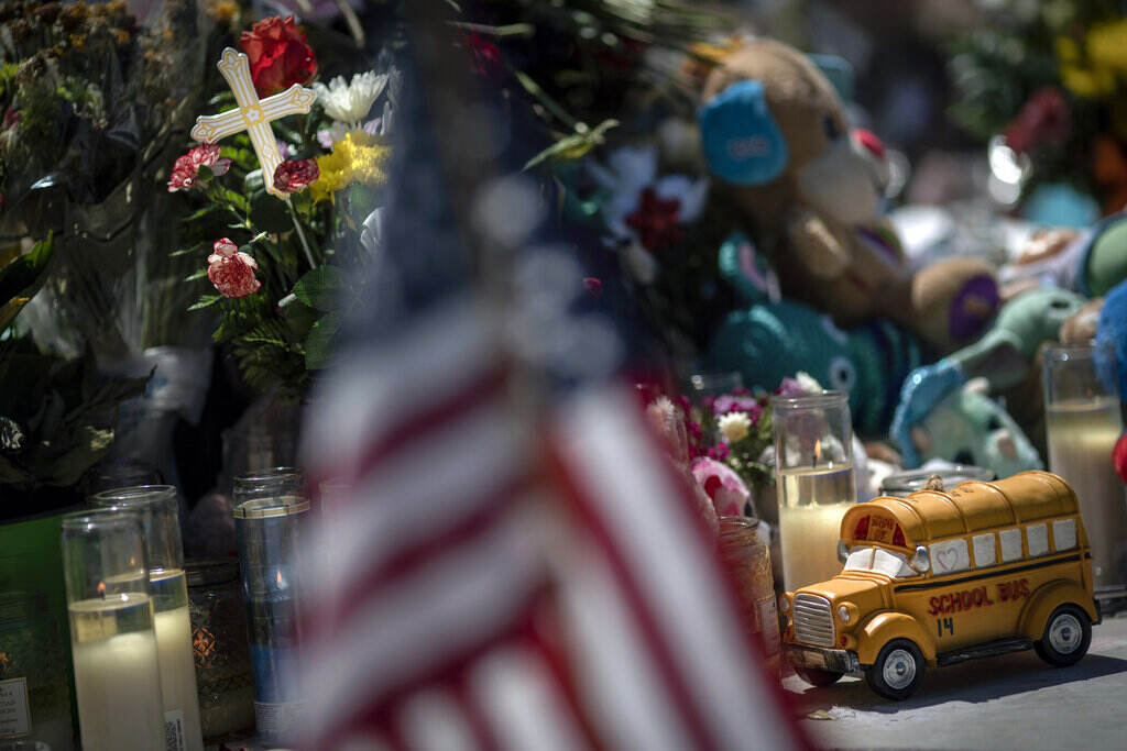 Texas School Shooting Empty Spaces A toy yellow school bus is in focus, with a blurry American flag in the foreground.