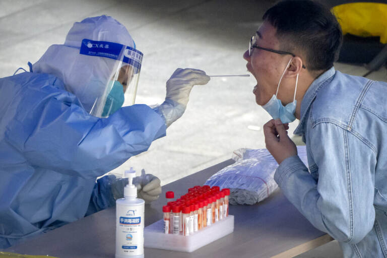 A worker in a protective suit swabs a man's throat for a COVID-19 test at a testing site in an office complex in Beijing, Friday, April 29, 2022. The World Health Organization on Thursday, May 5, 2022 is estimating that nearly 15 million people were killed either by the coronavirus or by its impact on overwhelmed health systems in the past two years, more than double the official death toll of 6 million.