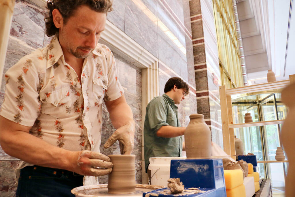 2022 06 07-e lee-benjamin peterson mike sullivan-philadelphia 3 logan square-plastic free philly wheel Benjamin Peterson (left) and Mike Sullivan throw clay in the lobby of 3 Logan Square in Center City. Over the course of seven weeks, they will create 156 handmade clay bottles as their contribution to the Plastic-free Philly campaign. (Emma Lee/WHYY)