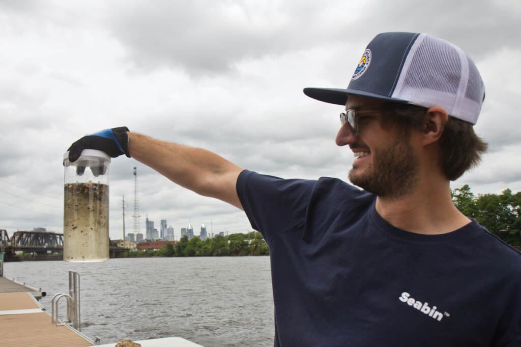 2022 06 07 k paynter epa micro plastics study (1 of 1)-3 Hayden Gould, Executive Project Manager, Seabin North America, holds up a container of micro plastics collected out of the Delaware River Watershed at a demonstration of their trash collecting devices at Bartrams’ Gardens on June 7, 2022. (Kimberly Paynter/WHYY)
