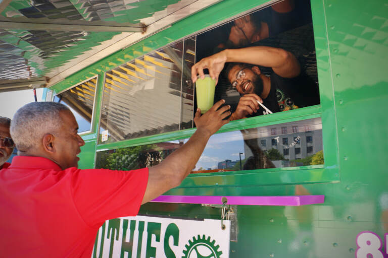 Victor Cobbs of The Green Machine food truck serves up a smoothie to Camden Mayor Vic Carstarphen. Food truck vendors can apply for seven licenses to operate in select locations under the city's pilot program. (Emma Lee/WHYY)