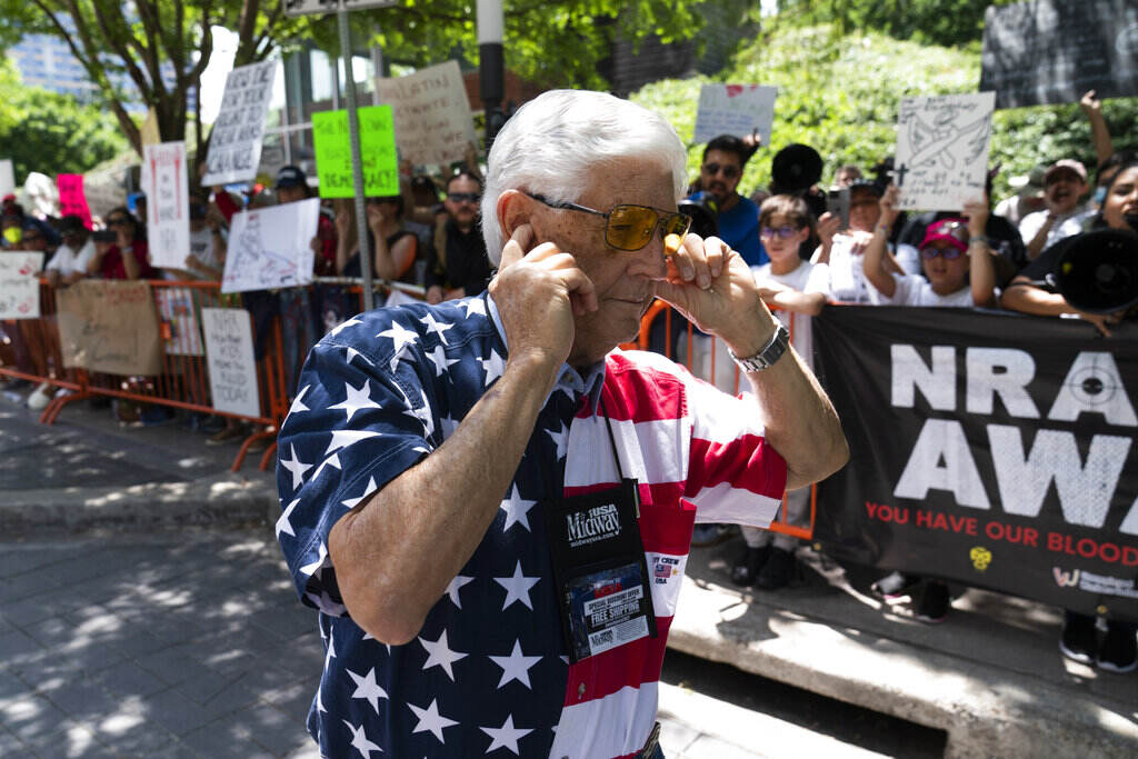 APTOPIX Texas School Shooting NRA A member of the National Rifle Association plugs his ears with his fingers as he walks past protesters during the NRA's annual meeting at the George R. Brown Convention Center