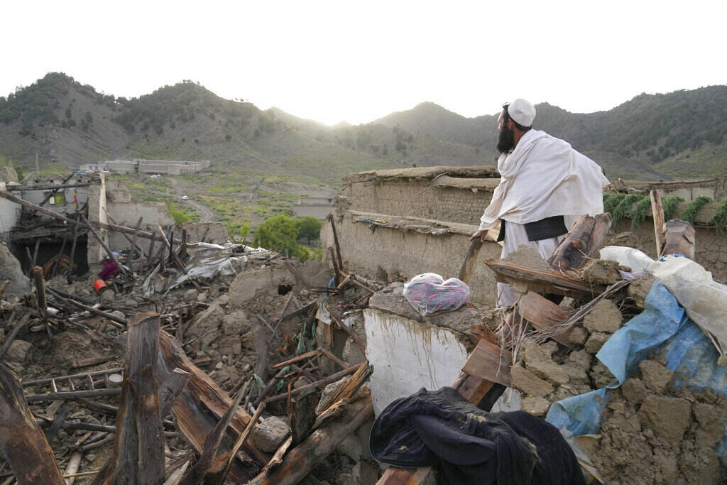 APTOPIX Afghanistan Earthquake A man stands looking out over destroyed buildings, with mountains in the distance.