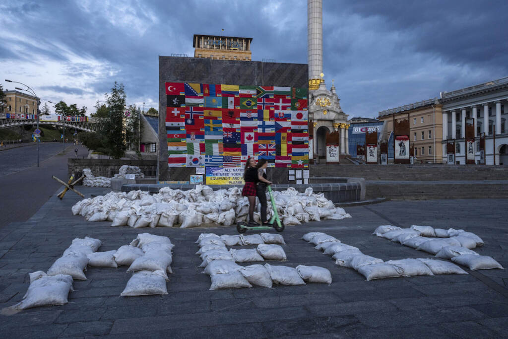 Russia Ukraine War Daily Life Women ride a scooter through Kyiv's Maidan Square, past sandbags that spell out 'HELP,' and flags displayed from around the world, in Ukraine, Saturday, June 25, 2022. (AP Photo/Nariman El-Mofty)