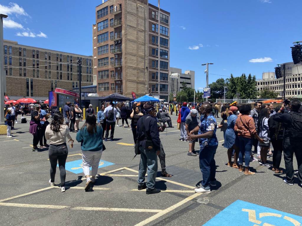 View of a crowd of people dancing in an open space with buildings in the background.
