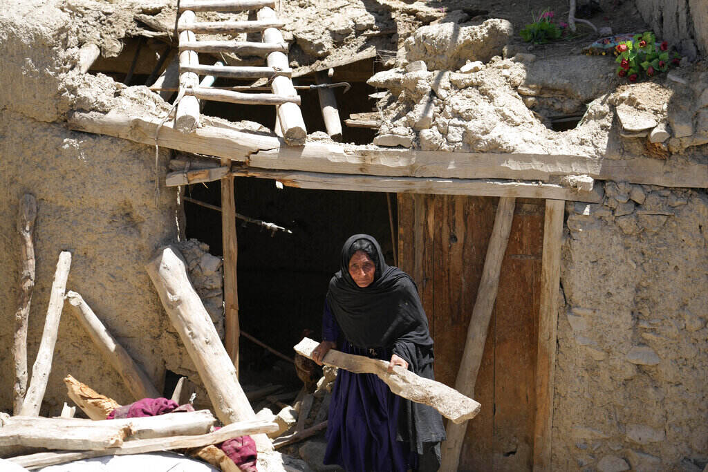 Afghanistan Earthquake A woman carries a piece of wood as she walks outside through the entrance of a damaged house.