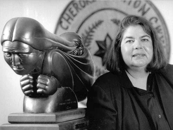 Wilma Mankiller is being honored with a new U.S. quarter. Portrait of Wilma Mankiller in black and white with a statue behind her.