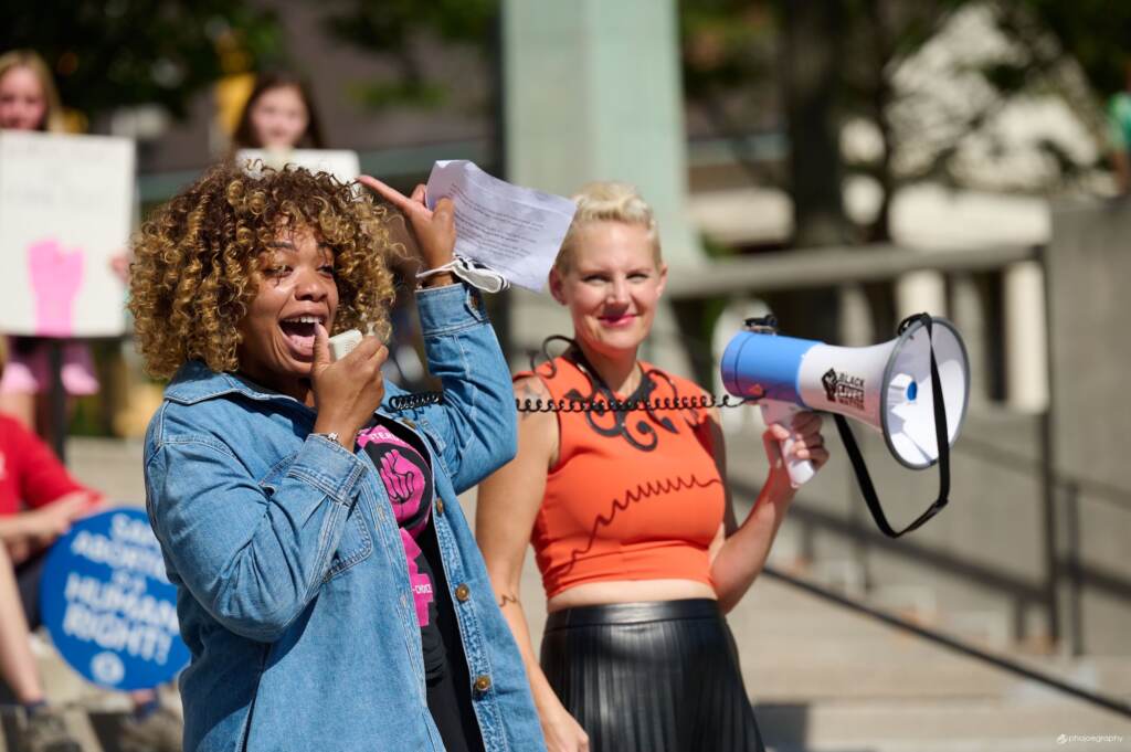 delaware-abortion-rights Rep. Minor-Brown talks into a microphone, as someone else behind her holds a megaphone in the air.