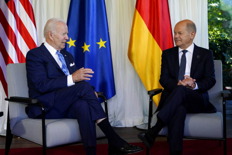 President Biden sits in a chair on the left, with Germany's Chancellor Olaf Scholz sits in a chair on the right, appearing to be listening to President Biden as he talks.