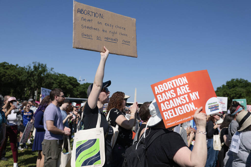 Activists Gather For Jewish Rally For Abortion Justice A protester holds up a sign supporting abortion rights in the midst of a crowd, with a blue sky in the background.