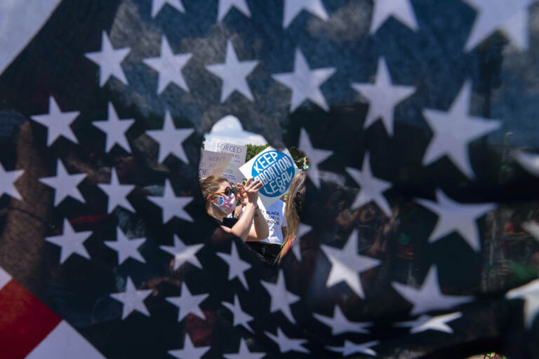 Abortion-rights activists are seen through a hole in an American flag as they protest outside the Supreme Court