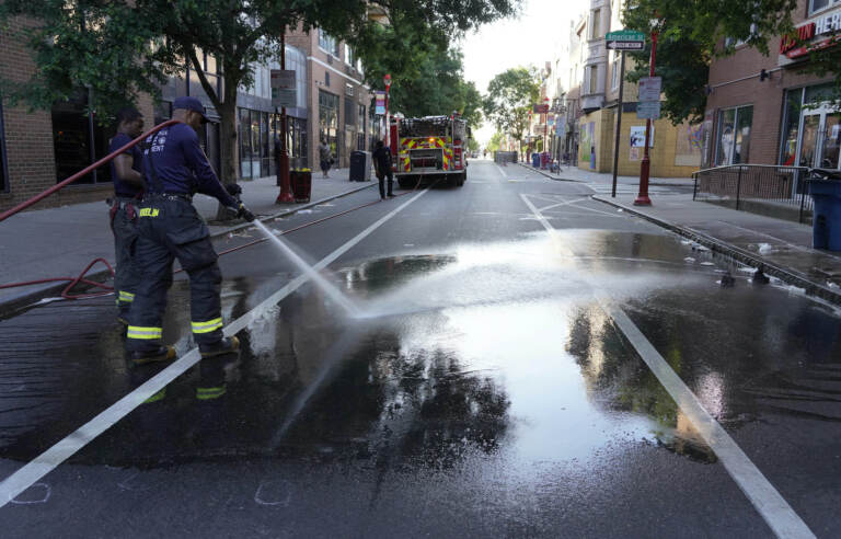 A Philadelphia firefighter washes blood off the sidewalk at the scene of a fatal overnight shooting on South Street in Philadelphia, Sunday, June 5, 2022. (AP Photo/Michael Perez)