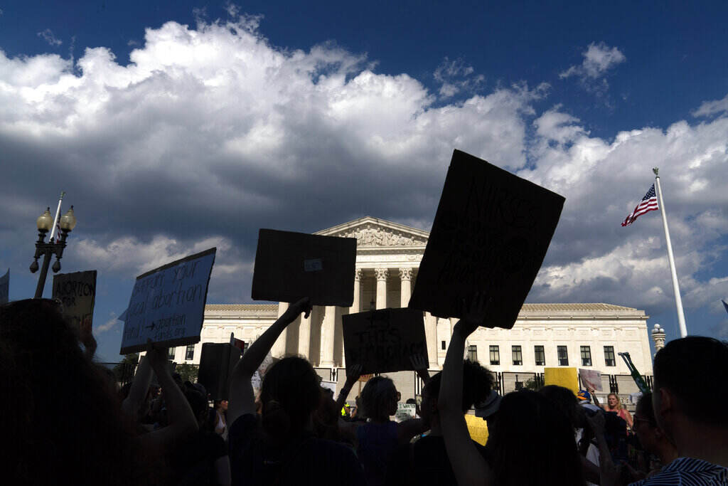 Supreme Court Silhouettes of the hands of different people in a crowd waving signs are visible in the foreground, with the U.S. Supreme Court building in the background.