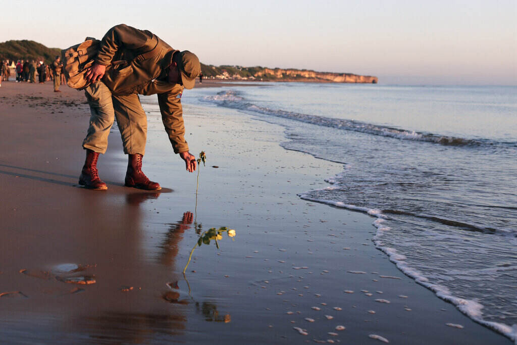 APTOPIX France D-Day Anniversary A WWII soldier re-enactor picks something up on the beach in Normandy.