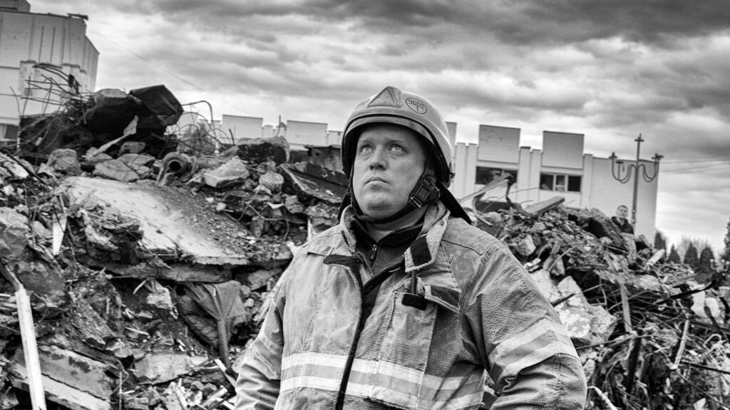 Ukraine War, 2022 A man in a firefighter suit looks up toward the sky. The photo is in black and white.