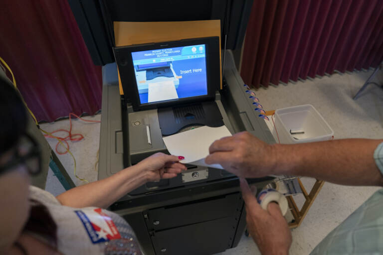 Two people guide a ballot into a machine.