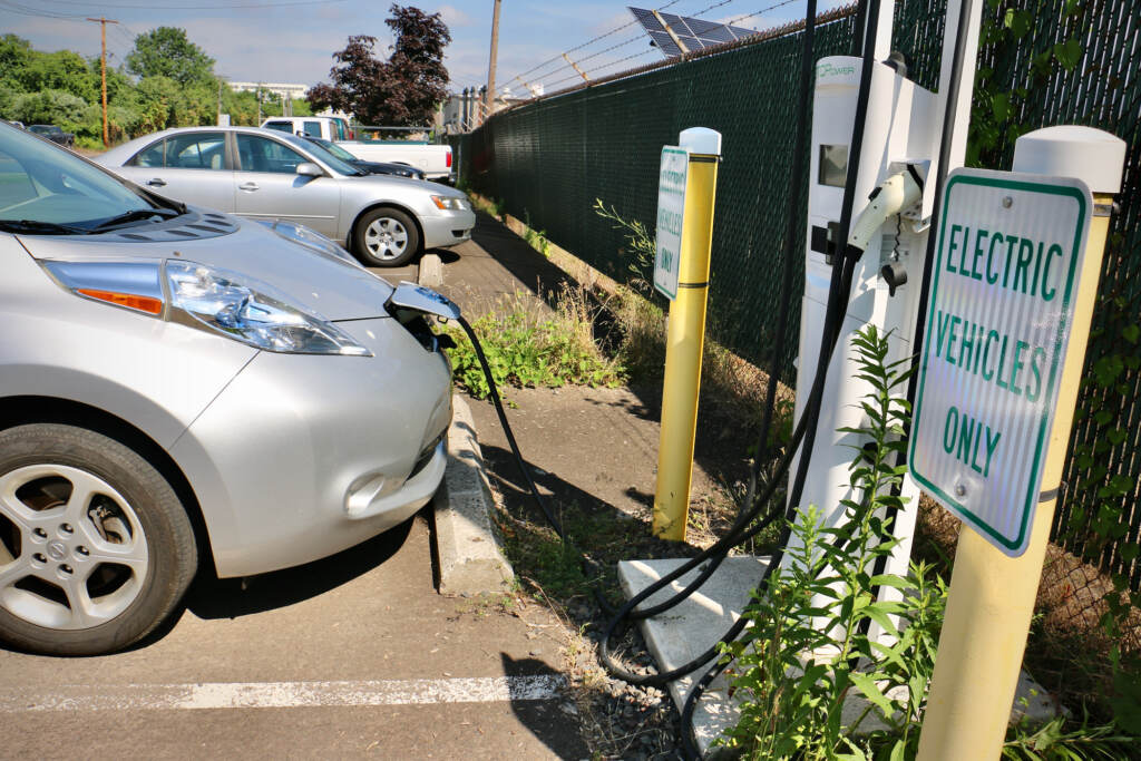 An electric charge is plugged into a charging station, next to a sign that reads, 