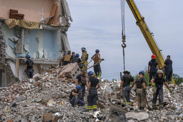Rescue workers in Ukraine stand on a pile of rubble.